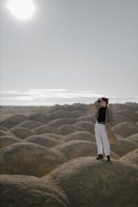 woman in white pants standing on brown sand